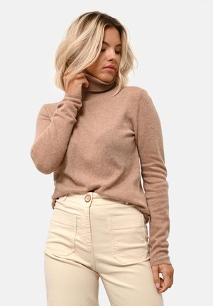 Beżowy sweter w stylu golf z miękkiego materiału o długich rękawach, zestawiony z jasnobeżowymi spodniami o wysokim stanie z zapięciem na guzik.