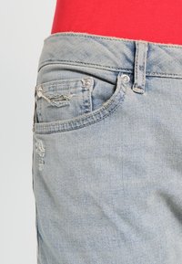 Vaqueros de denim azul claro con un diseño desgastado, estilo de cinco bolsillos, presillas para cinturón y herrajes en tono plateado en la cinturilla.