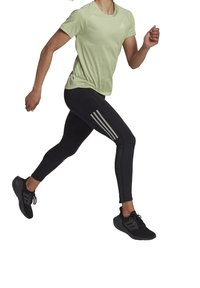 Jasnozielona sportowa koszulka z krótkimi rękawami i teksturowanym wzorem, zestawiona z czarnymi legginsami z trzema białymi paskami po bokach.