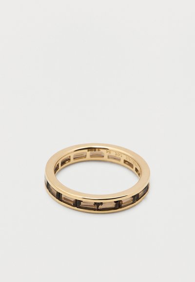 Aranyszínű gyűrű, sima szalaggal, téglalap alakú kivágásokkal, amelyek sötét belső részeket láttatnak. Csiszolt felületű, modern kialakítású.