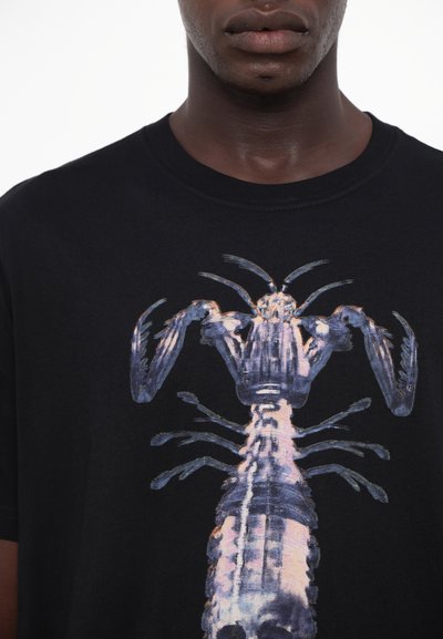 T-shirt noir arborant un grand graphisme détaillé de homard multicolore sur le devant ; manches courtes et encolure ronde.