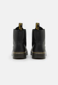 Black leather ankle boots with rounded toes, yellow stitching along the sole, and black rubber soles. Features pull tabs for easy wear.