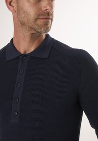 Dunkelblaues Strickpoloshirt mit strukturiertem Finish, ausgestattet mit einem spitzen Kragen und sechs Knöpfen auf der Vorderseite.