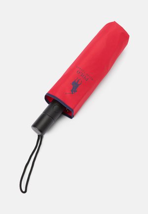 Umbrelă pliabilă roșie cu mâner negru, având accente albastre și un design cu logo. Include o husă de transport asortată cu curea de mână.