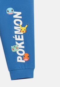 Μπλε ύφασμα με το κείμενο "Pokémon" και πολύχρωμα πρόσωπα Pokémon: Squirtle, Pikachu, Bulbasaur και Charmander διατεταγμένα κατακόρυφα.