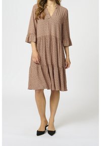 Vestido marrón con estampado de manchas, escote en V, mangas tres cuartos, diseño con volantes y dobladillo con volantes, combinado con zapatos negros. Textura de tela suave.