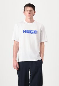 Hvid bomulds t-shirt med et blåt "HUGO" grafisk print på brystet. Korte ærmer og en afslappet pasform, med en glat tekstur.