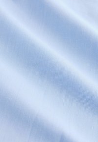 Tissu bleu clair à texture fine en côtes diagonales, plié doucement créant des ombres et des reflets délicats.