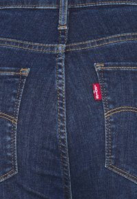 Mörkblå denimjeans med gyllene sömmar, med två bakfickor och en röd Levi's-logotyp på den högra fickan.