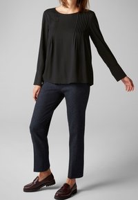 Blusa nera a maniche lunghe con dettagli plissettati frontalmente, abbinata a pantaloni scuri dalla texture e mocassini bordeaux.