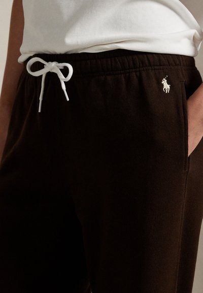 Primo piano di pantaloni della tuta neri con coulisse bianca annodata a fiocco e piccolo logo ricamato di giocatore di polo vicino al bordo della tasca.