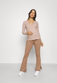 Gestreiftes Langarmshirt in Weiß und Rost mit V-Ausschnitt und elastischer Passform. Braune Schlaghosen mit Seitenschlitzen und gerippter Textur. Weiße Sneakers.
