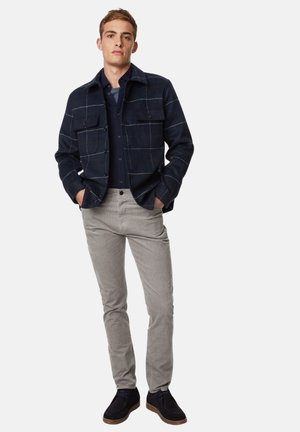 Marineblå ternet jakke med forlommer, båret over en marineblå skjorte, parret med lysegrå bukser og mørke sko. Enkel, struktureret design.