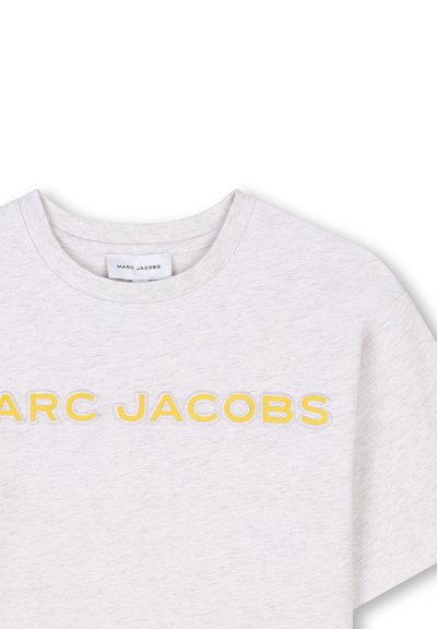 T-shirt en coton gris clair avec un col rond et des manches courtes, portant "MARC JACOBS" brodé en jaune sur le devant.