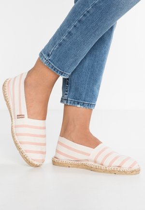Fødder iført pink og hvide stribede espadriller med jutesåler, kombineret med cropped blå denimjeans på hvid baggrund.