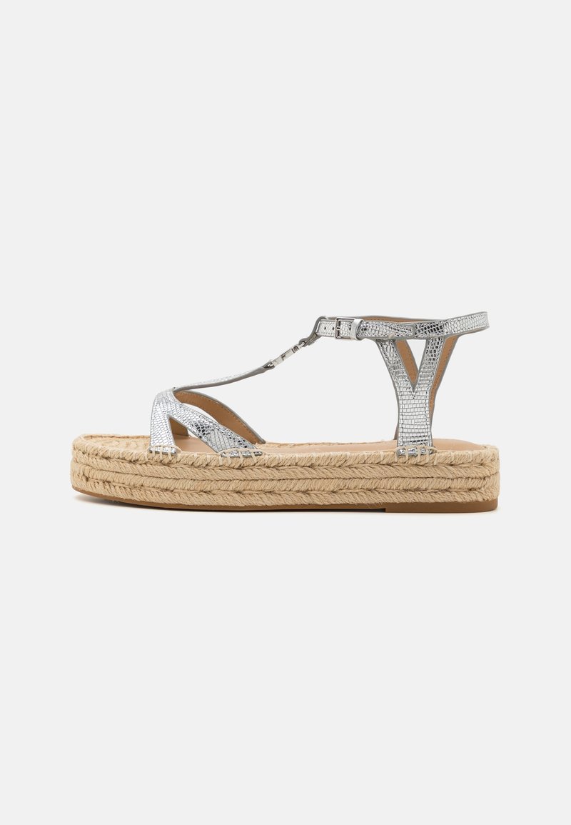 Silver metallisk T-strap sandal med spänne, texturerad ovandel och tjock flätad jutesula mot en vit bakgrund.