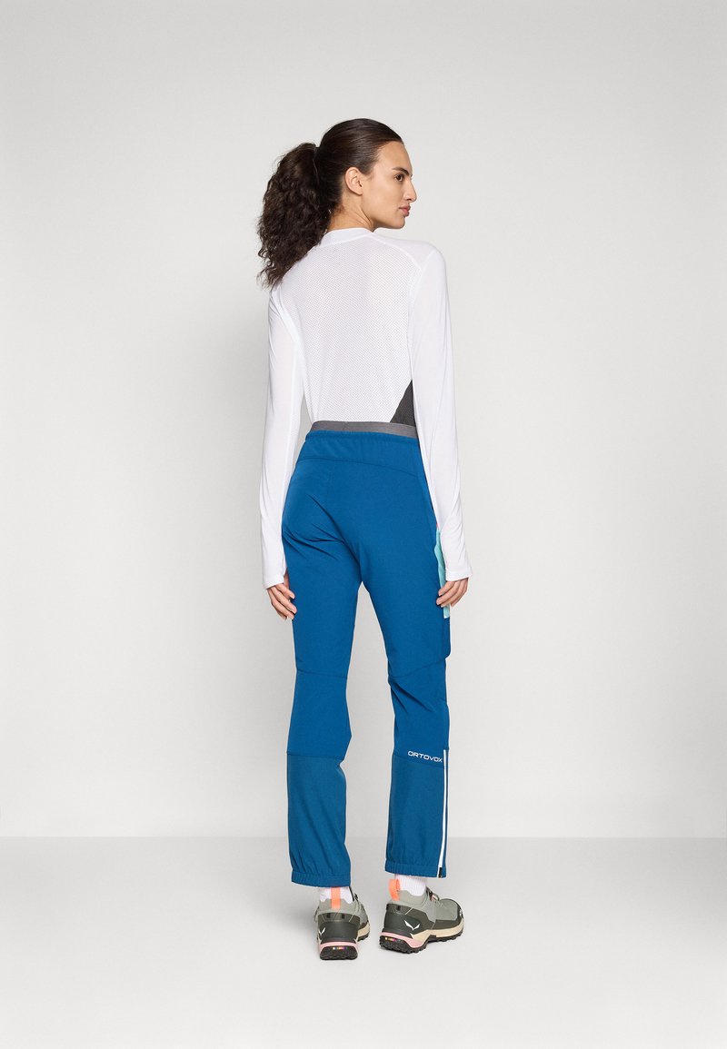 Damen-Sportbekleidungs-Outfit, bestehend aus einem weißen Langarmoberteil mit Mesh-Rücken und blauen Hosen mit Seiteneinsätzen und elastischem Bund.