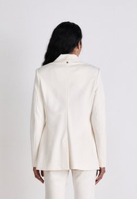 White tailored blazer with a single back vent and minimalistic design. Features a button detail at the neck and straight silhouette.