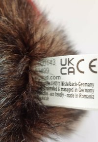 Brown furry fabric with a white label displaying UKCA and CE compliance marks and manufacturing details in Germany and Romania.