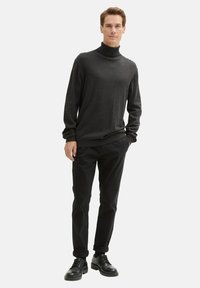 Czarny sweter z golfem o miękkiej fakturze, zestawiony z czarnymi spodniami i czarnymi sznurowanymi butami, prezentujący casualowy wygląd.