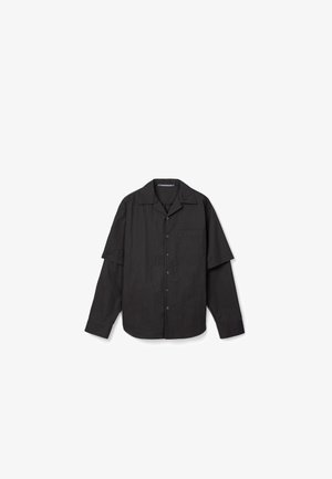 Chemise noire à manches longues avec boutons, manches courtes superposées et poche poitrine, présentée sur fond blanc.