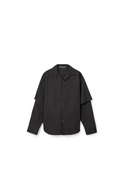 Camisa negra de manga larga con botones, mangas cortas superpuestas y un bolsillo en el pecho, mostrada sobre un fondo blanco.