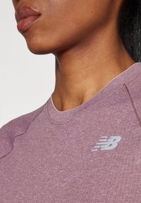 Ljuslila kortärmad topp med en rundhalsringning. Har textilstruktur och en grå New Balance-logotyp på bröstet.