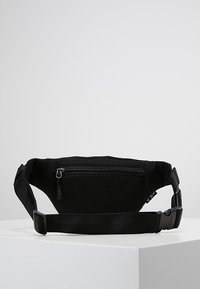 Svart mesh midjeväska med en frontfack med dragkedja, justerbart bälte och logotag. Har en strukturerad yta för ventilation.