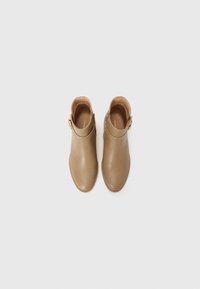 Bottes de cheville beiges avec une finition en cuir lisse, bout rond et un détail de boucle dorée sur le côté. Semelle texturée pour une meilleure adhérence.