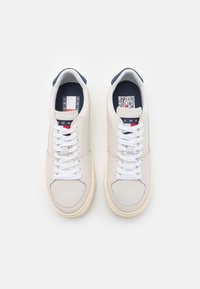 Zapatillas de cuero beige con cordones blancos, punta redonda y un acento en navy en el talón. Presentan una plantilla con logo y un código QR.