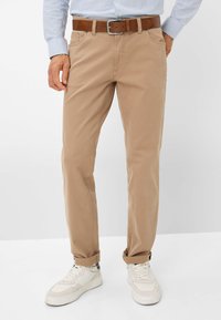 Beige katoenen chinos met een reguliere pasvorm, voorzien van twee voorzakken en een brown leren riem. Draag met witte sneakers.