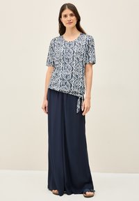 Abito lungo blu navy con un design leggero e fluttuante; abbinato a una maglietta a maniche corte a fantasia con forme geometriche blu e bianche.