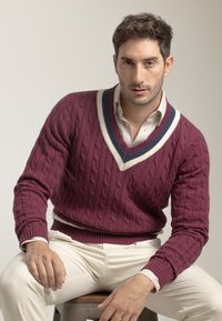 Suéter de punto de cable burdeos con escote en V, que presenta rayas blancas y navy. Combinado con pantalones ajustados color crema.