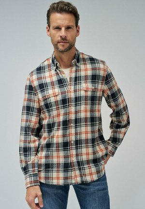 Camisa de franela a cuadros en colores azul marino, crema y óxido. Diseño de botones con dos bolsillos en el pecho, mangas largas y un cuello clásico.