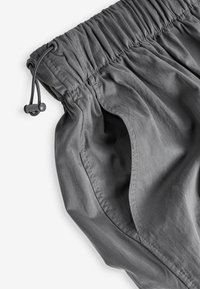 Shorts gris avec une taille élastique et un cordon de serrage, dotés de poches latérales. Texture douce avec un léger éclat, mettant en valeur un tissu léger.