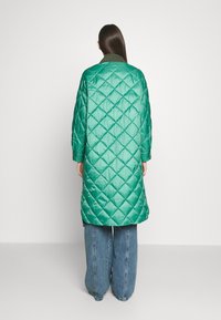 Cappotto lungo verde trapuntato con finitura lucida, dotato di colletto e maniche oversize, abbinato a pantaloni in denim blu dal fit morbido.