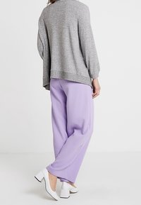 Šedý oversized svetr s dlouhými rukávy, doplněný o světle fialové kalhoty. Boty jsou bílé s robustním podpatkem. Hladké textury a uvolněný střih.