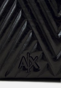 Borsa nera trapuntata realizzata in materiale lucido; presenta motivi diagonali e il logo impresso "A|X" nella parte inferiore. Texture liscia.