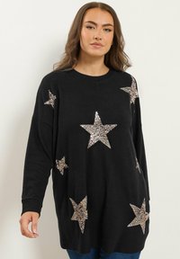 Pull noir à manches longues avec de grandes étoiles argentées en sequins. Coupe ample avec un col rond et un tissu texturé.
