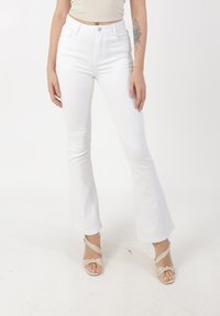 White flared jeans with a high waist, made of denim. Features a single button closure, belt loops, and a smooth texture.