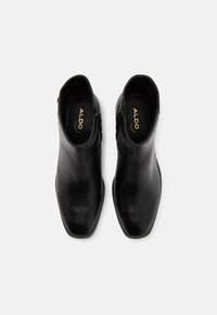 Bottines en cuir noir avec un design à bout pointu, finition lisse et fermeture à glissière sur le côté, comportant le nom de la marque "ALDO" à l'intérieur.