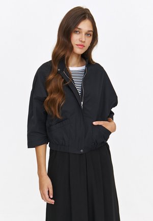 Czarna skrócona kurtka z wysokim kołnierzem, zamkiem błyskawicznym i dwiema przednimi kieszeniami. Wykonana z lekkiego materiału o lekko fakturowanym wykończeniu.