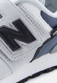 Γκρι σουέντ αθλητικό παπούτσι με μαύρο δερμάτινο λογότυπο, υφασμάτινες σκούρες μπλε λεπτομέρειες, λευκά πλέγματα και πολύχρωμη σόλα με κηλίδες.