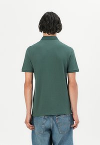 Polo shirt vert à manches courtes avec un col classique, en coton doux, aux lignes épurées et à la texture lisse. Vue arrière montrant un design ajusté.