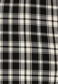 Černobílá kostkovaná tkanina s mřížkovým vzorem a různou tloušťkou pruhů, hladkým povrchem a konzistentním barevným kontrastem.