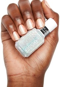 Bouteille de vernis à ongles Essie avec une base transparente et des paillettes iridescentes, tenue dans une main avec des ongles courts fraîchement manucurés, teinte rose clair.