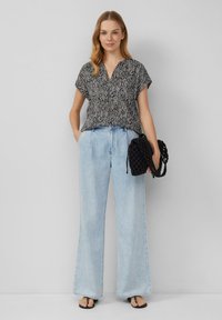 Schwarz-weißer gemusterter kurzärmeliger Oberteil kombiniert mit hellblauen weiten Jeans; das Model hält eine schwarze geflochtene Handtasche.
