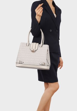 Donna in abito blazer blu navy che tiene una borsa beige con motivo, dotata di doppi manici e dettagli con fibbia.