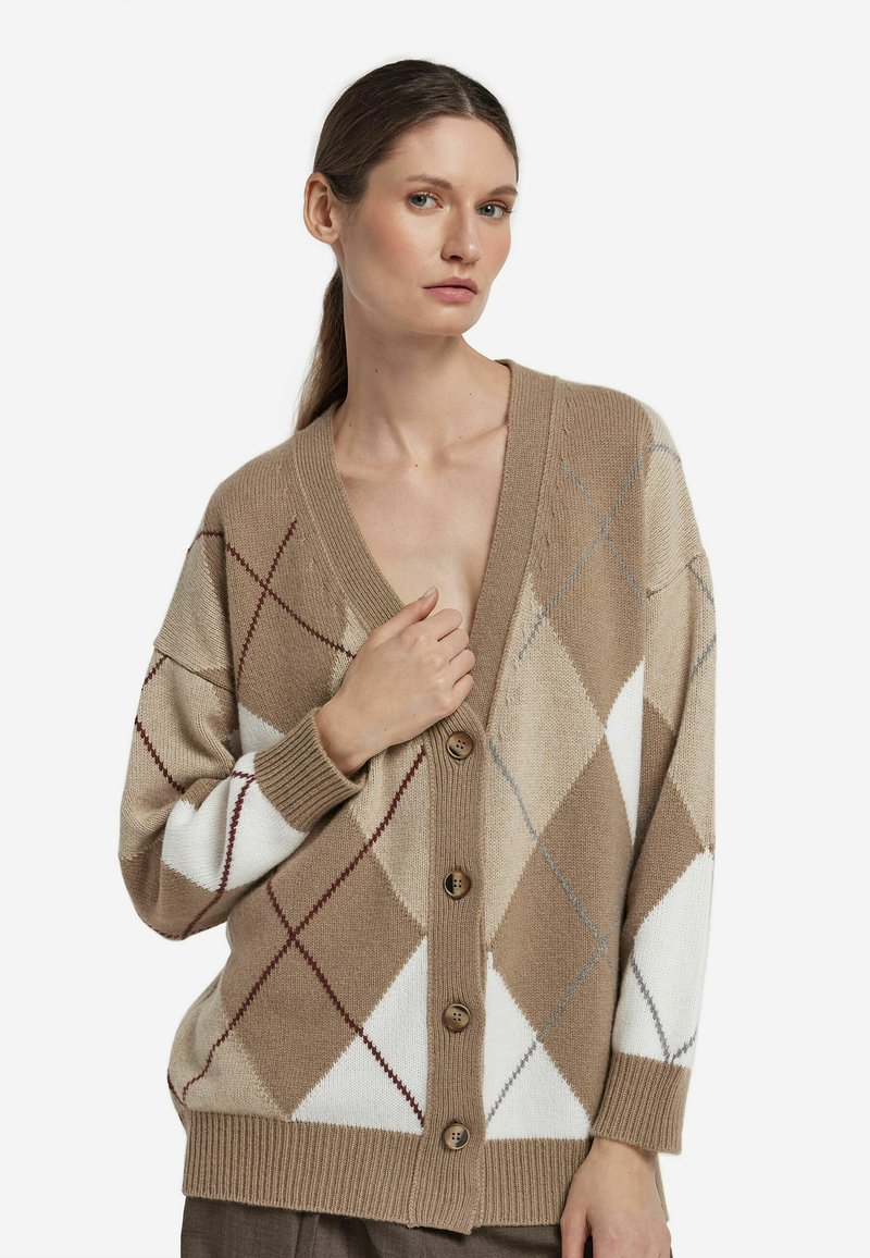 Beżowy kardigan w wzór argyle z brązowymi, białymi i czerwonymi diamentami. Miękki materiał dzianinowy, dekolt w serek, zapięcie na guziki i ściągane mankiety.