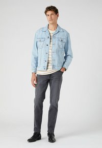 Jasnoniebieska kurtka dżinsowa z dwoma kieszeniami na piersiach, z zapięciem na guziki, długimi rękawami i luźnym krojem. Połączona z prążkowaną koszulą i ciemnoszarymi spodniami.